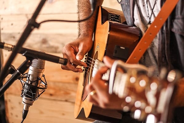 Close up image of man playing acoustic guitar with two vintage microphones