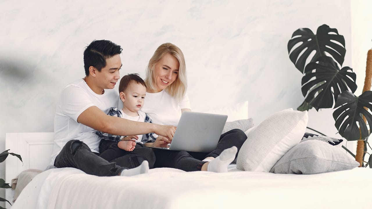 family of three sitting in bed looking at computer