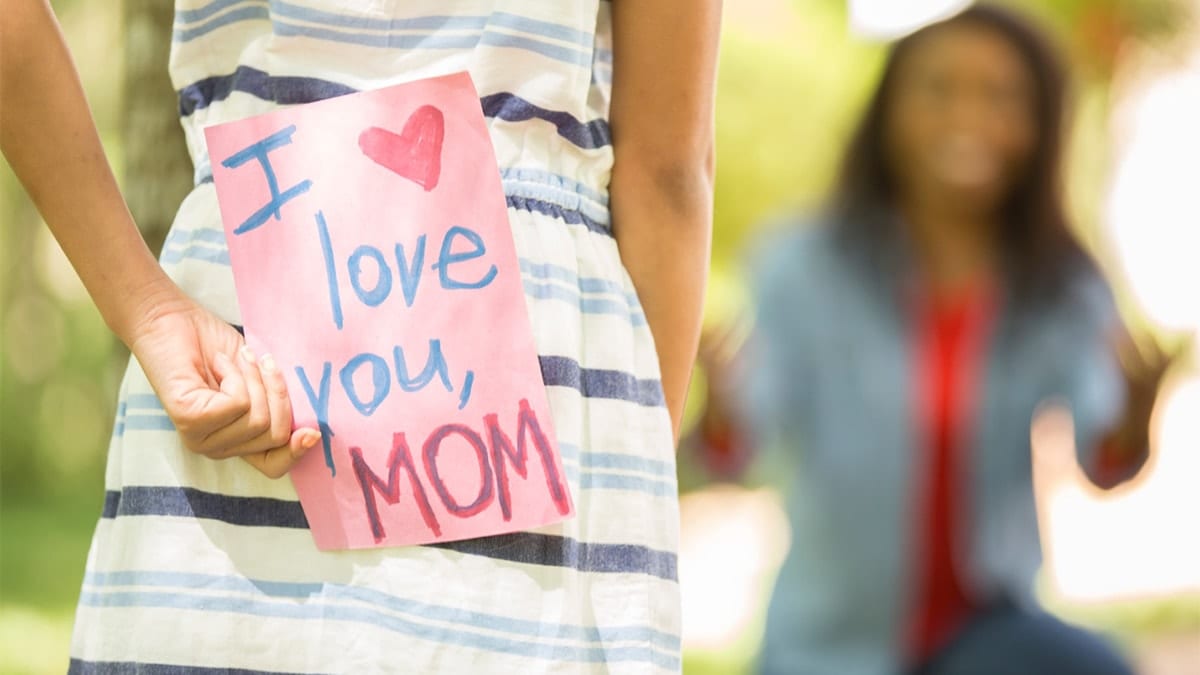 girl holding a sign saying "i love you mom" behind her back
