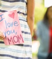 girl holding a sign saying "i love you mom" behind her back