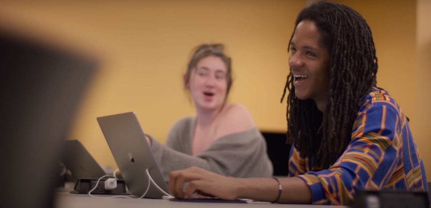 Two students smiling while creatinf content on macbook pros