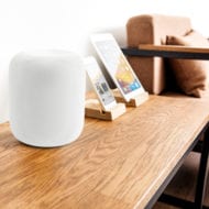 White Apple HomePod on a table next to an iPhone and iPad